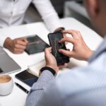 Business professionals using smartphones and tablets to analyze trading charts during a meeting.