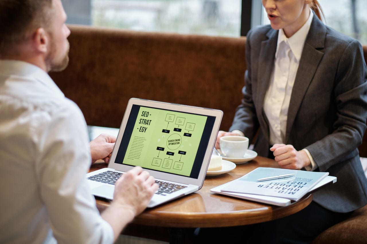 about-me A man and woman engaged in a business meeting discussing SEO strategy in a cozy cafe setting.